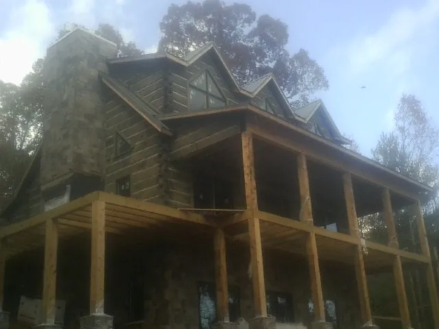 Stone chimney and dormers on a large log home with a timber porch in New Castle